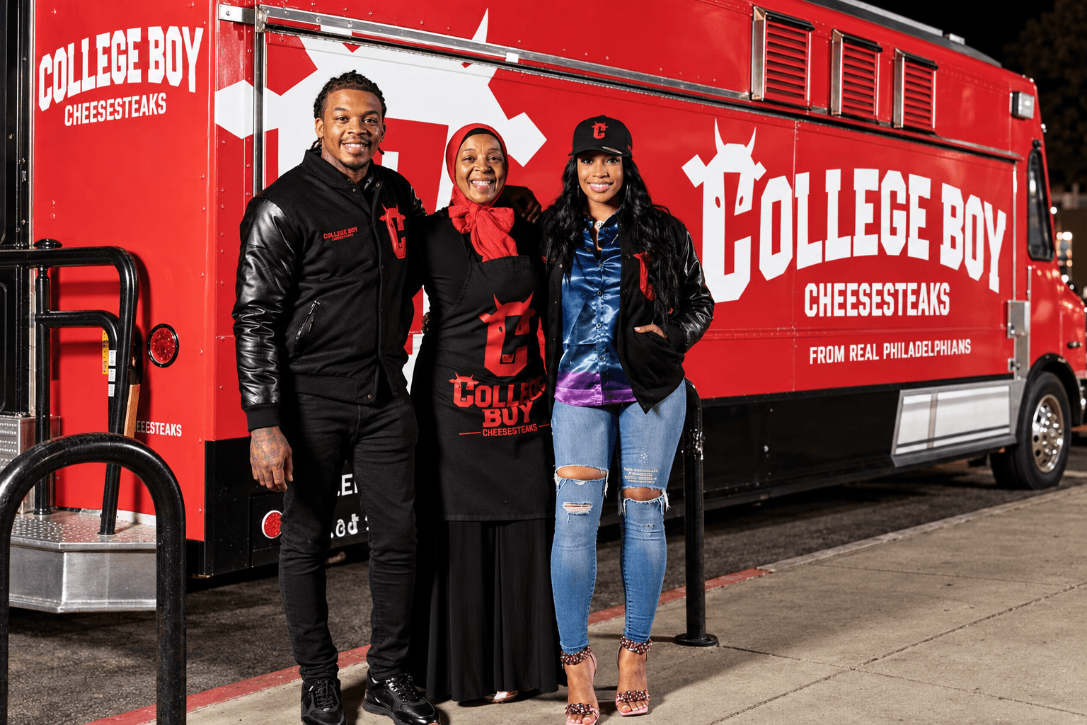 The family owners of College Boy Cheesesteaks standing together in front of the red food truck